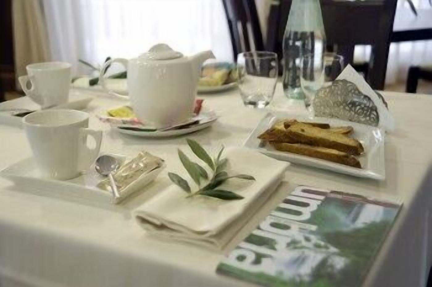 A neatly arranged breakfast table with a teapot, cups, a glass, and a plate of toast.
