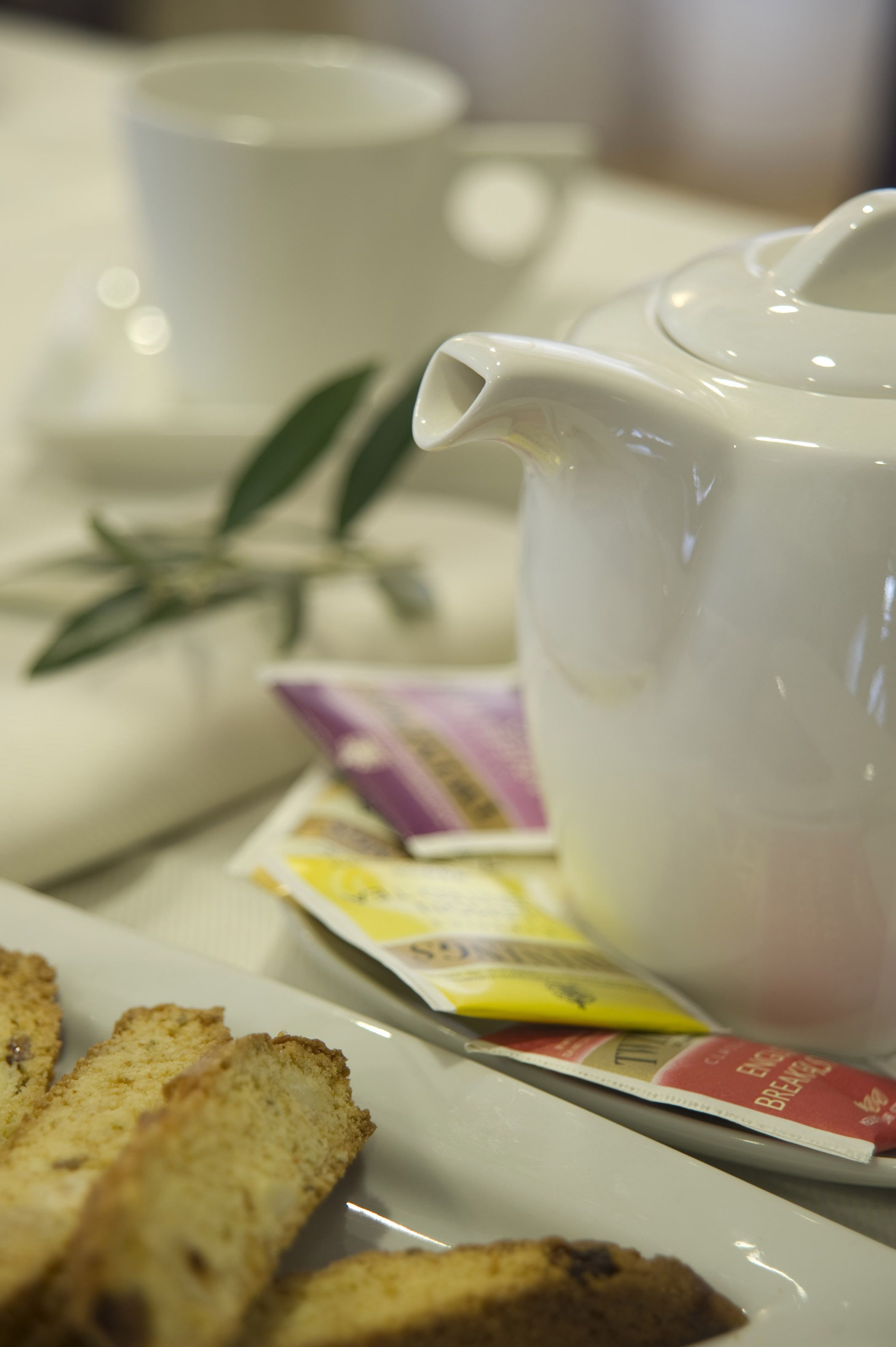 Una tetera blanca, una taza, un plato con tostadas y un sobre de té sobre una mesa.