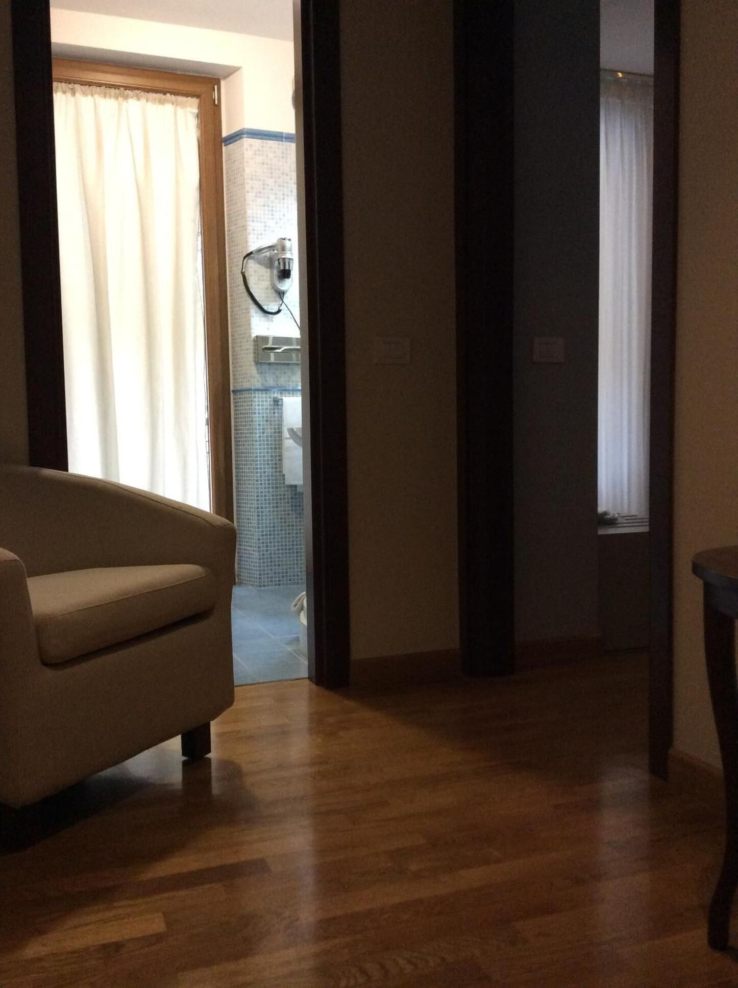 Quarto com piso de madeira, sofá bege e porta que dá para um banheiro com chuveiro e toalha pendurada na parede.