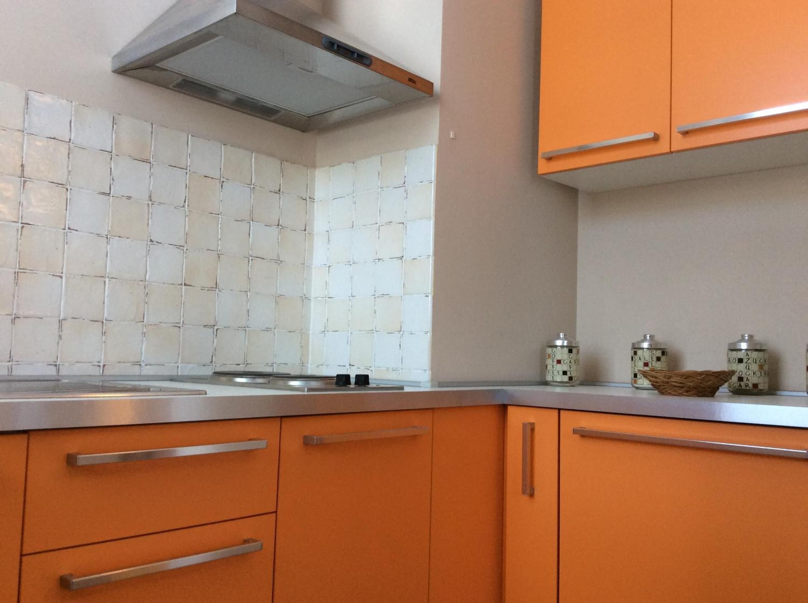 A kitchen with orange cabinets, a stainless steel countertop, and a tiled backsplash.