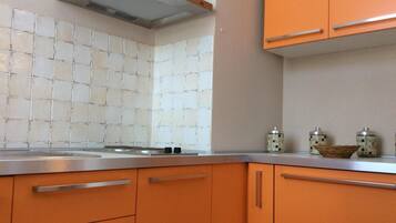 A kitchen with orange cabinets, a stainless steel countertop, and a tiled backsplash.