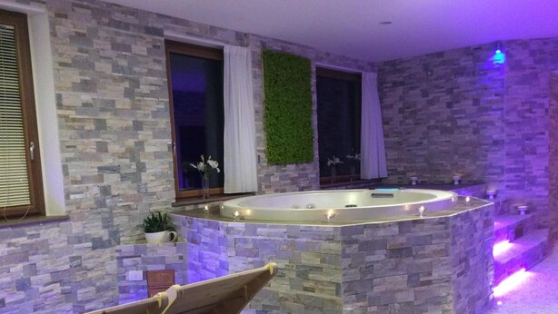 Un área de spa con una pared de piedra, un banco de madera y una bañera de hidromasaje.