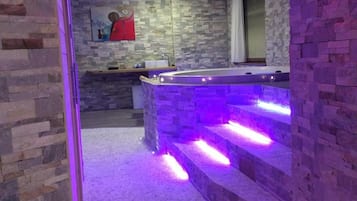 A spa area with a stone wall, a red towel, and a bathtub with purple lighting.