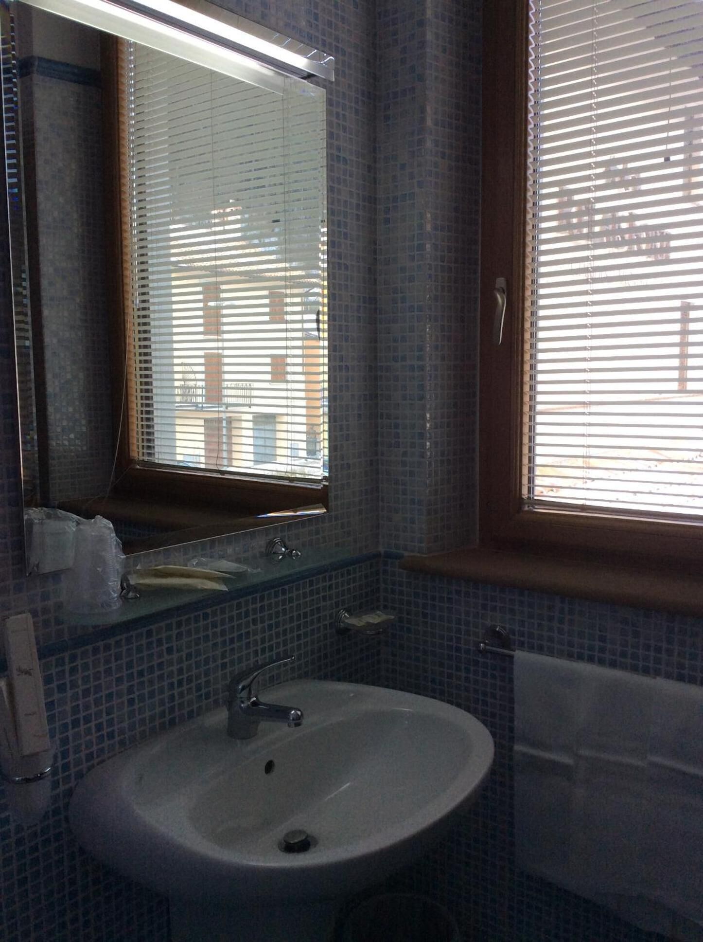 Ein Badezimmer mit Waschbecken, Spiegel und Fenster mit Jalousien.