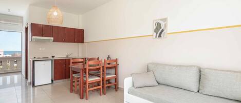 Una sala moderna con un sofá gris, una mesa de comedor de madera y sillas. En primer plano, una pequeña mesa blanca con un objeto decorativo.