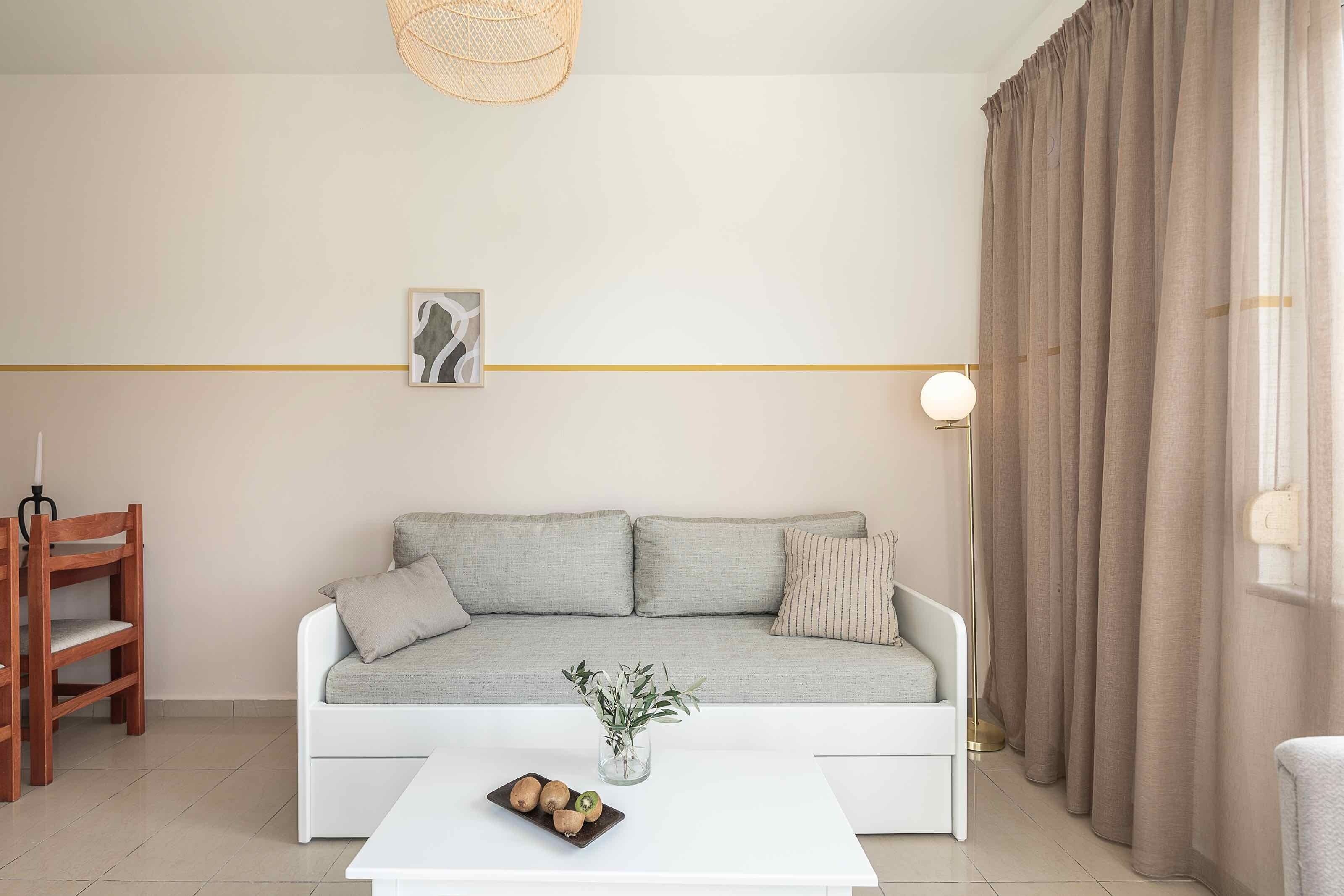 A modern living room with a grey sofa, a white coffee table, a wooden chair, and a vase with green plants.