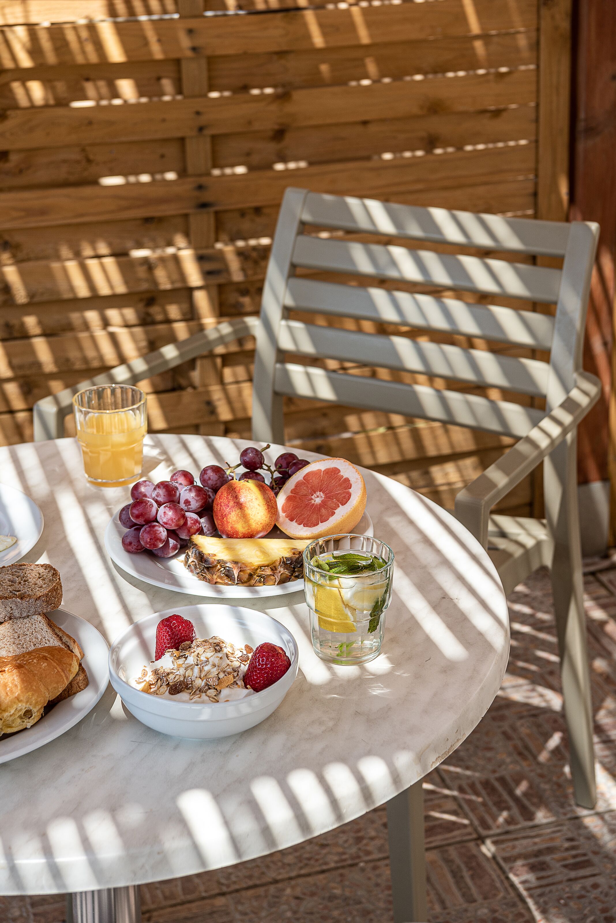 A table set with breakfast items including toast, fruit, and a glass of juice, with a wooden fence in the background.