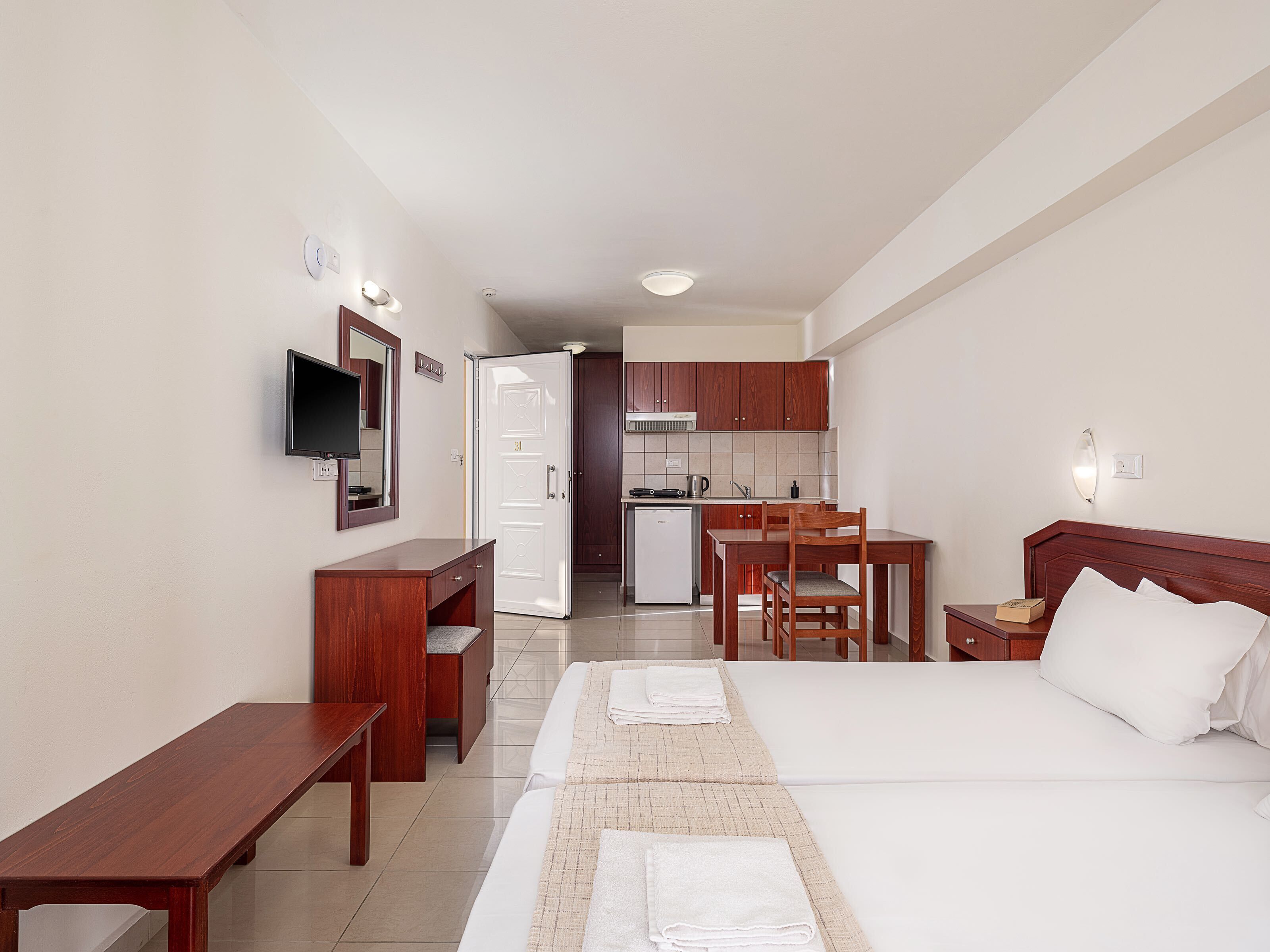 A hotel room with a bed, a desk, a chair, a television, and a kitchenette.