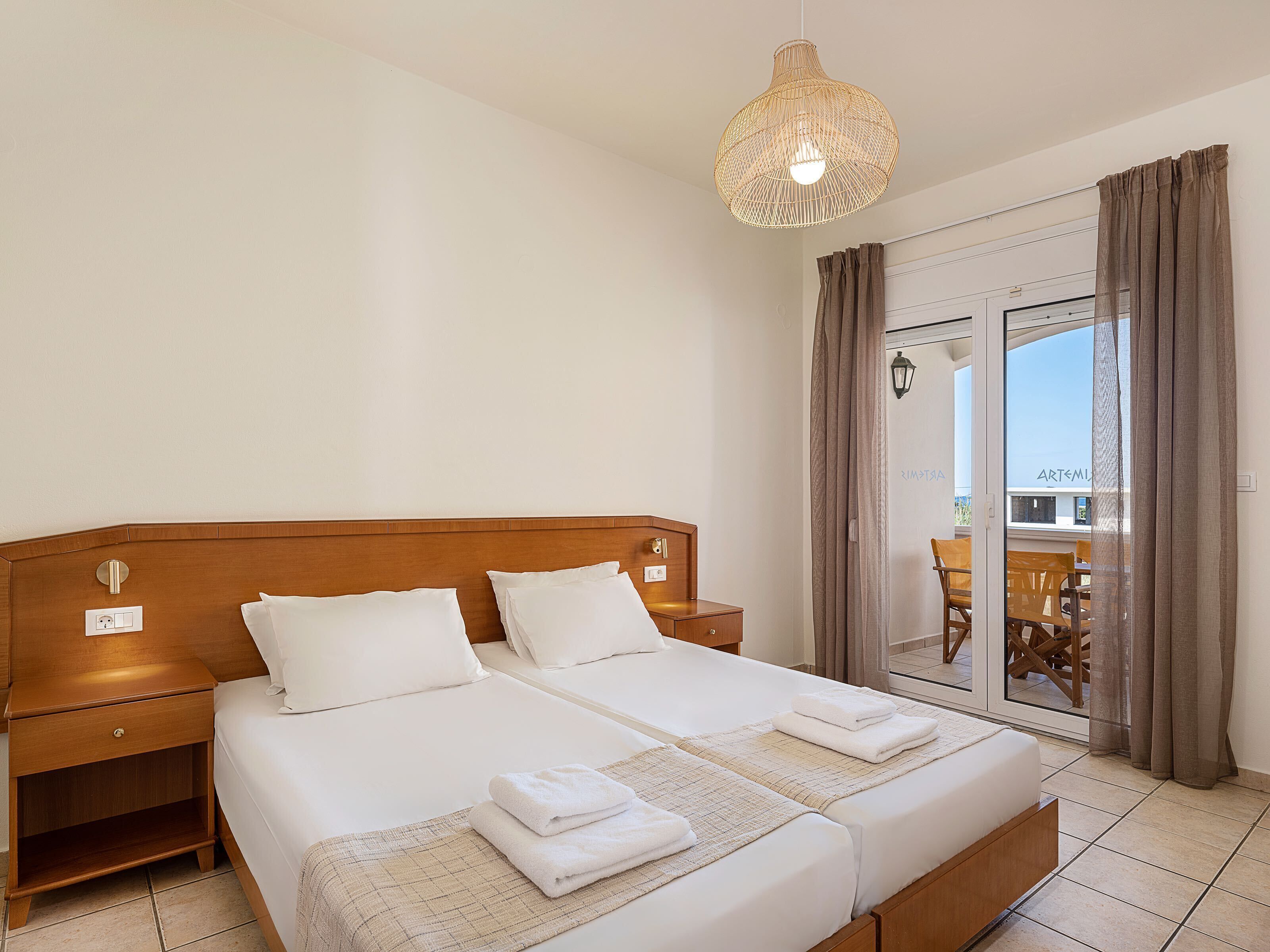 A hotel room with a large bed, two bedside tables, a wooden headboard, and a balcony with a view of the city.
