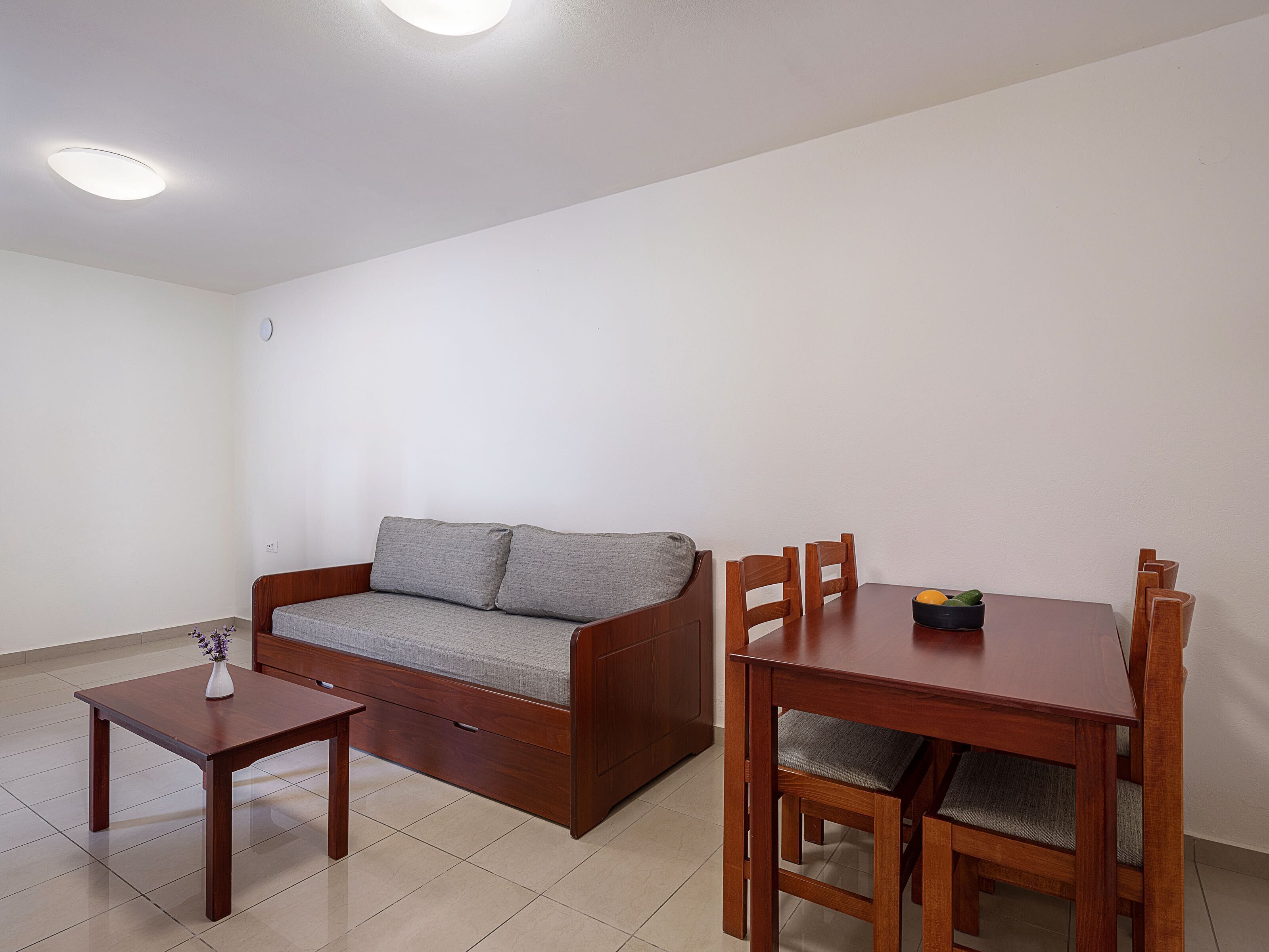 Una sala de estar con un sofá, una mesita de madera y una mesa de comedor con sillas.