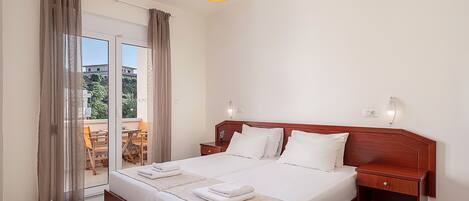 A hotel room with a large bed, wooden headboard, two bedside tables, a nightstand, a balcony with a table and chairs, and a hanging light fixture.