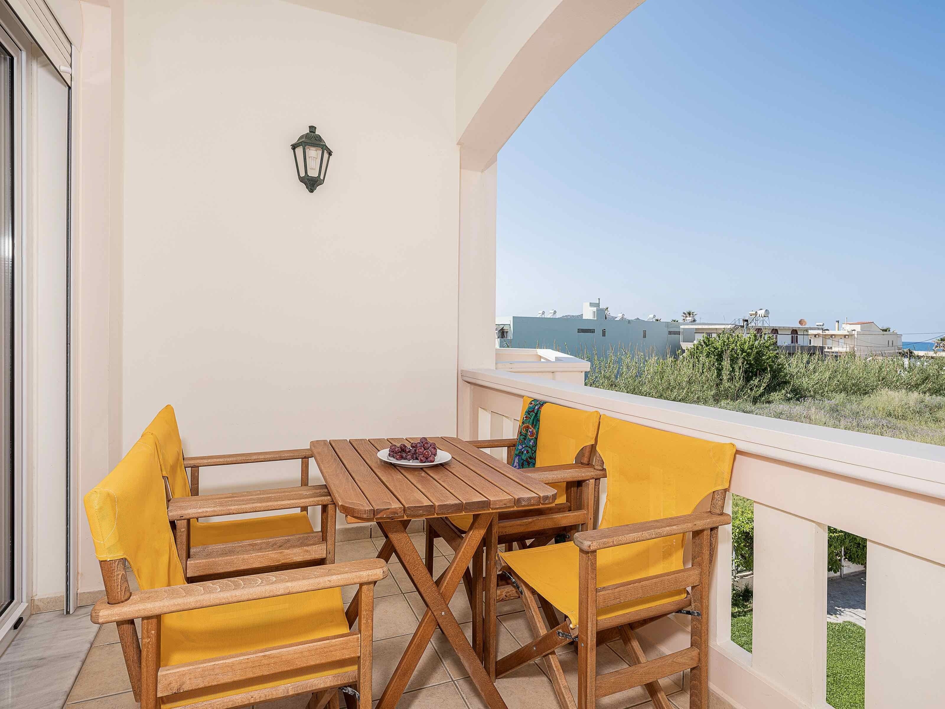 A balcony with a wooden table and chairs, a wall-mounted light, and a view of buildings in the distance.