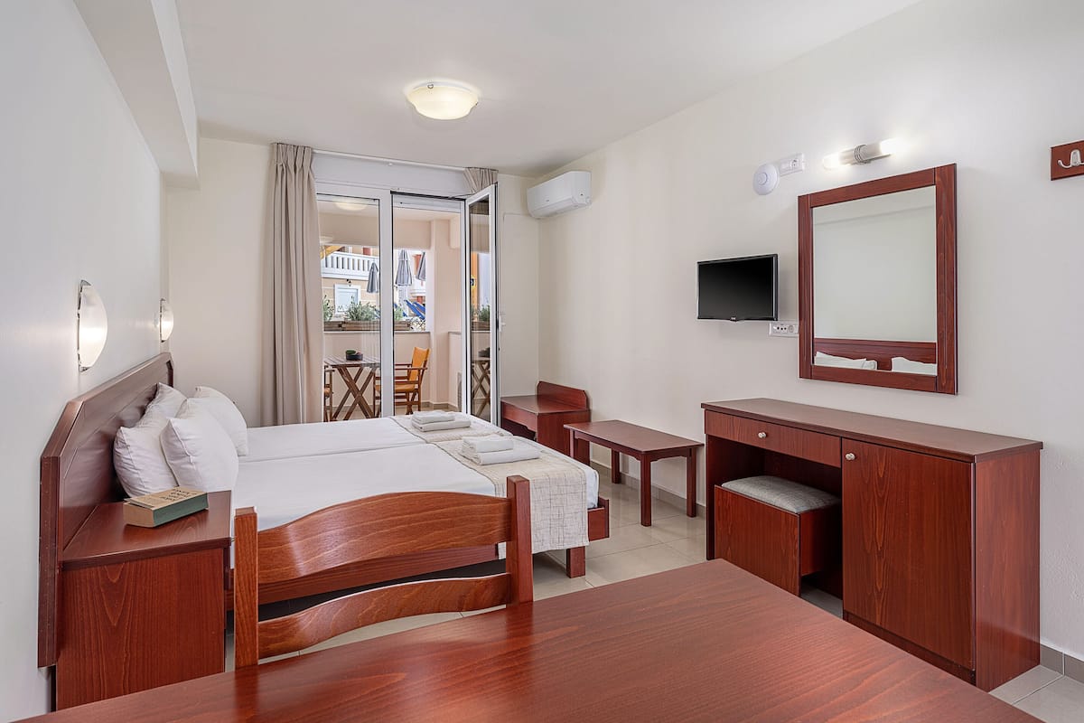A hotel room with a bed, a desk, a chair, a TV, and a bathroom mirror.