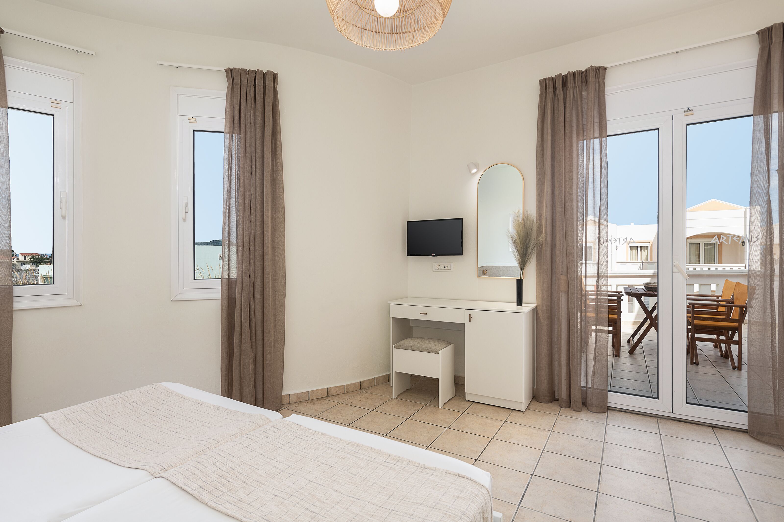 A hotel room with a bed, a desk with a TV, a mirror, and a view of the outside.