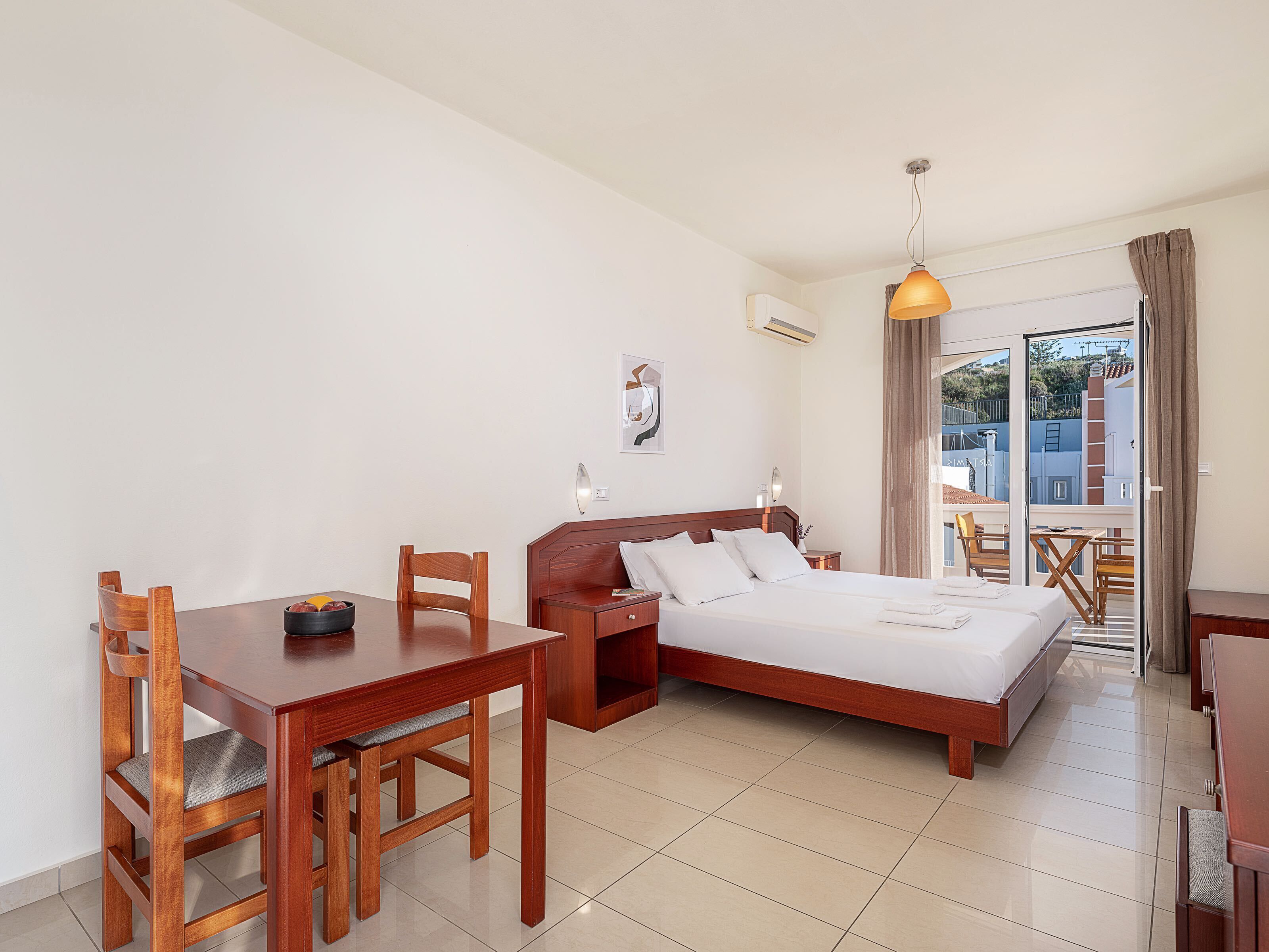 A hotel room with a bed, a wooden desk, a chair, and a dining table.