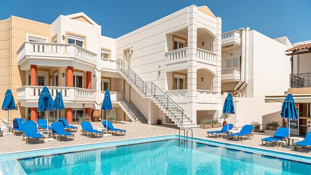 A swimming pool with blue lounge chairs and umbrellas, surrounded by a building with balconies and a staircase. - Artemis Apartments (Chania)