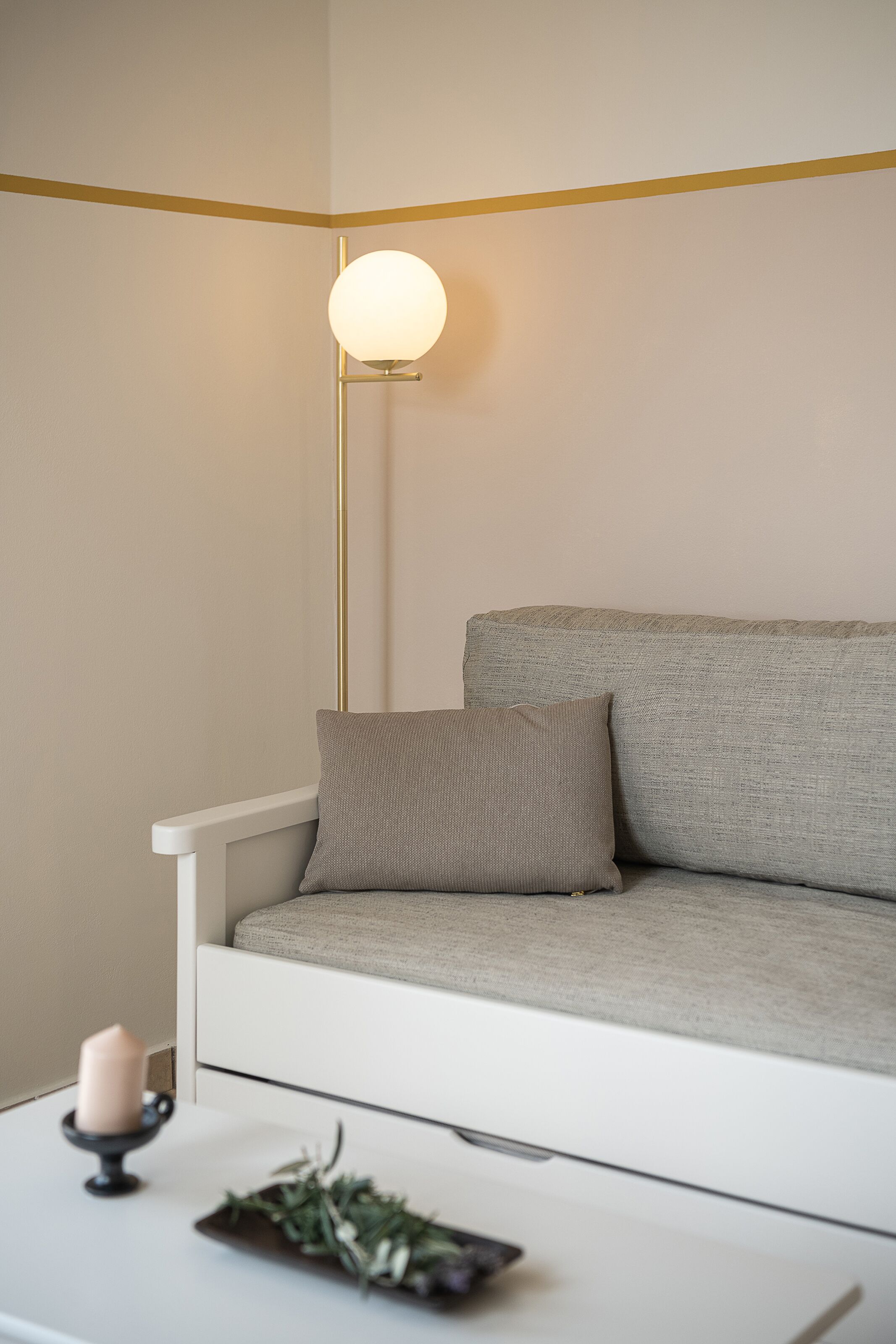 A minimalist living room with a sofa, a floor lamp, a small table with a candle, and a decorative plant.