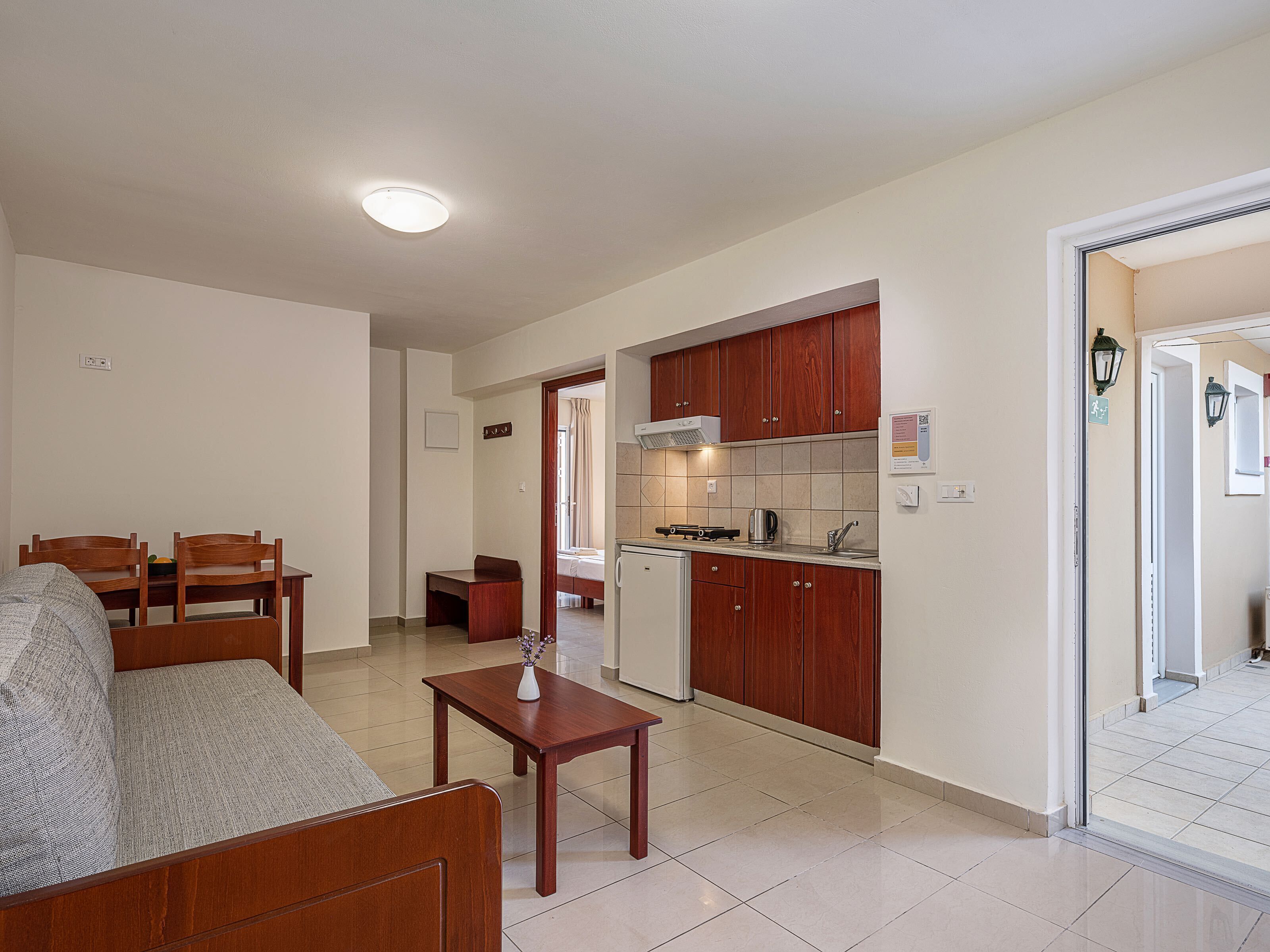 Un espacio habitable compacto con sofá, mesa de comedor, zona de cocina con armarios de madera y una pequeña kitchenette.