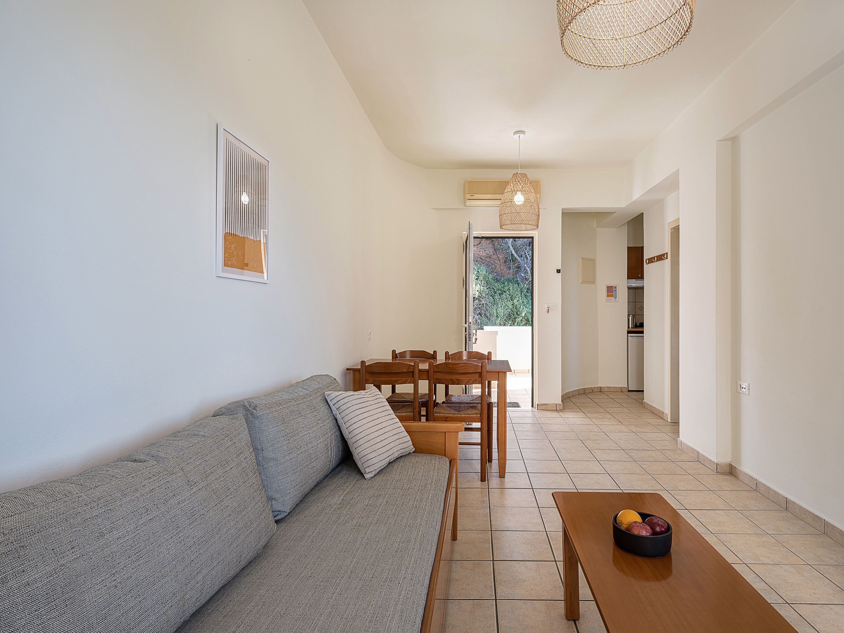 A modern living room with a grey sofa, wooden dining table, and a hanging light fixture.