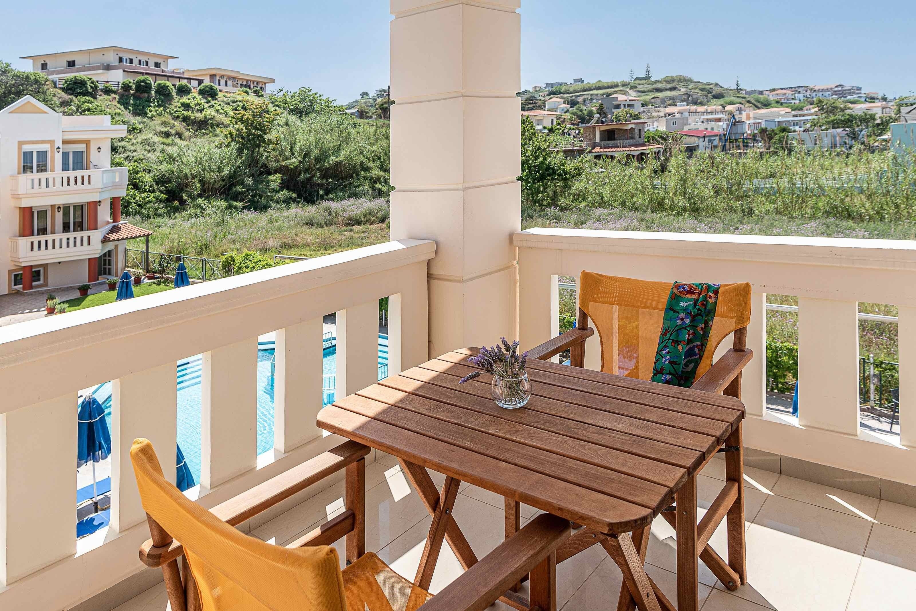 Una mesa de madera con sillas y un jarrón de flores en un balcón con vistas a una colina y edificios.