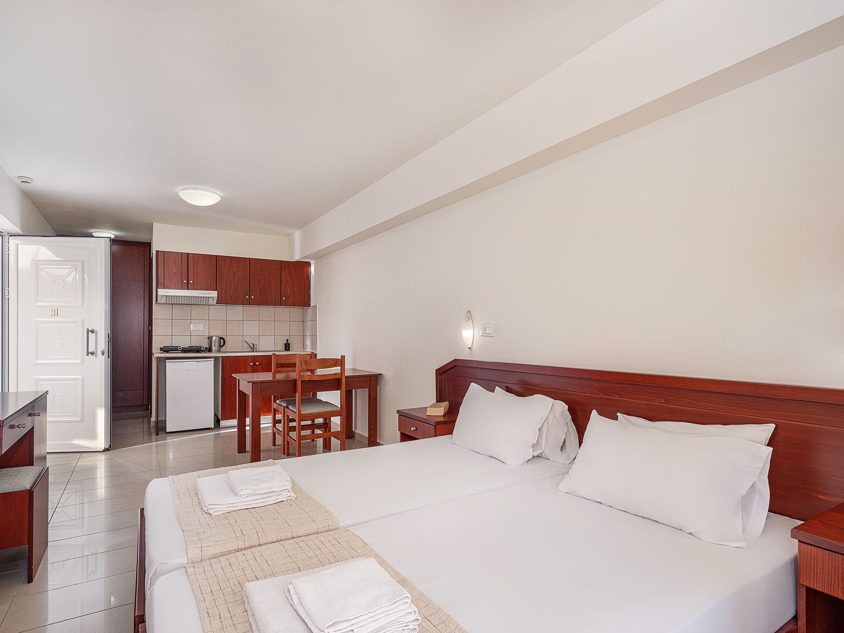 A hotel room with a bed, bedside table, and a small kitchenette.