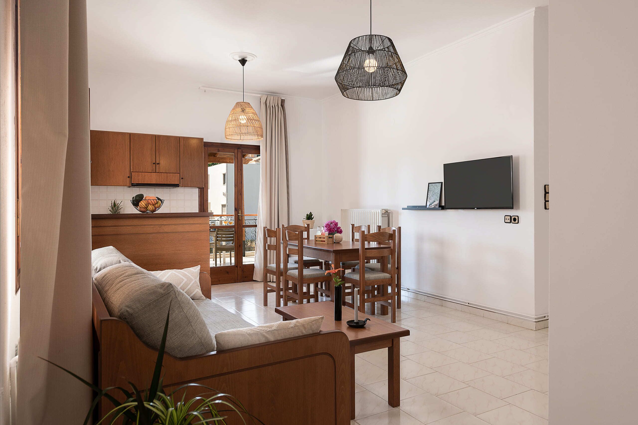 A modern living room with a sofa, dining table, chairs, and a TV mounted on the wall.