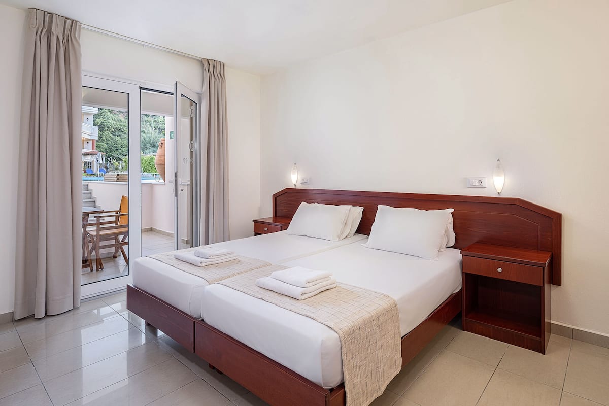 A hotel room with a large bed, a wooden nightstand, a bedside table, and a view of the outside balcony.