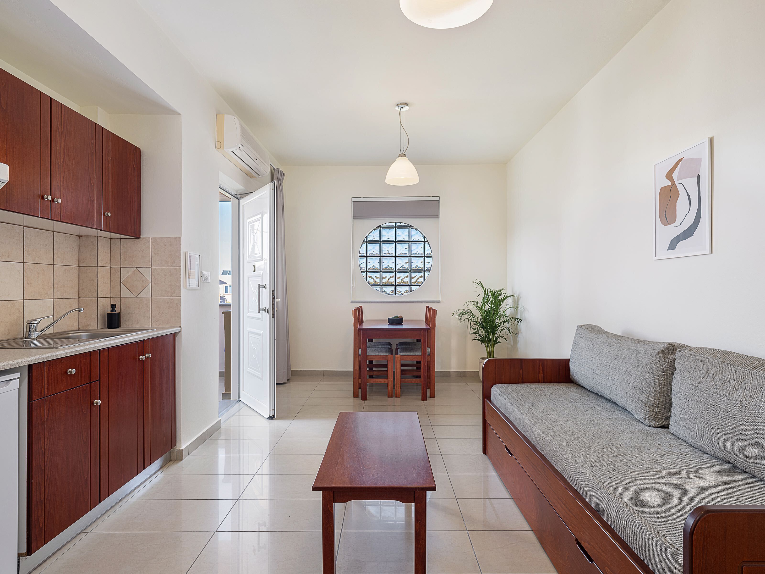 A modern kitchen with wooden cabinets, a dining area with a table and chairs, and a living area with a sofa.