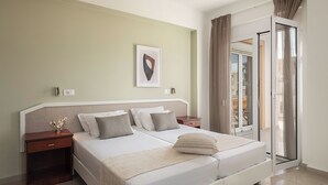 A hotel room with a bed, a nightstand, a wall-mounted light, a framed picture, and a sliding glass door to the outside. - Artemis Apartments (Chania)