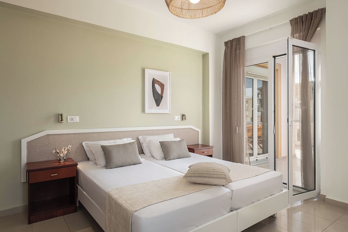 A hotel room with a bed, a nightstand, a wall-mounted light, a framed picture, and a sliding glass door to the outside.