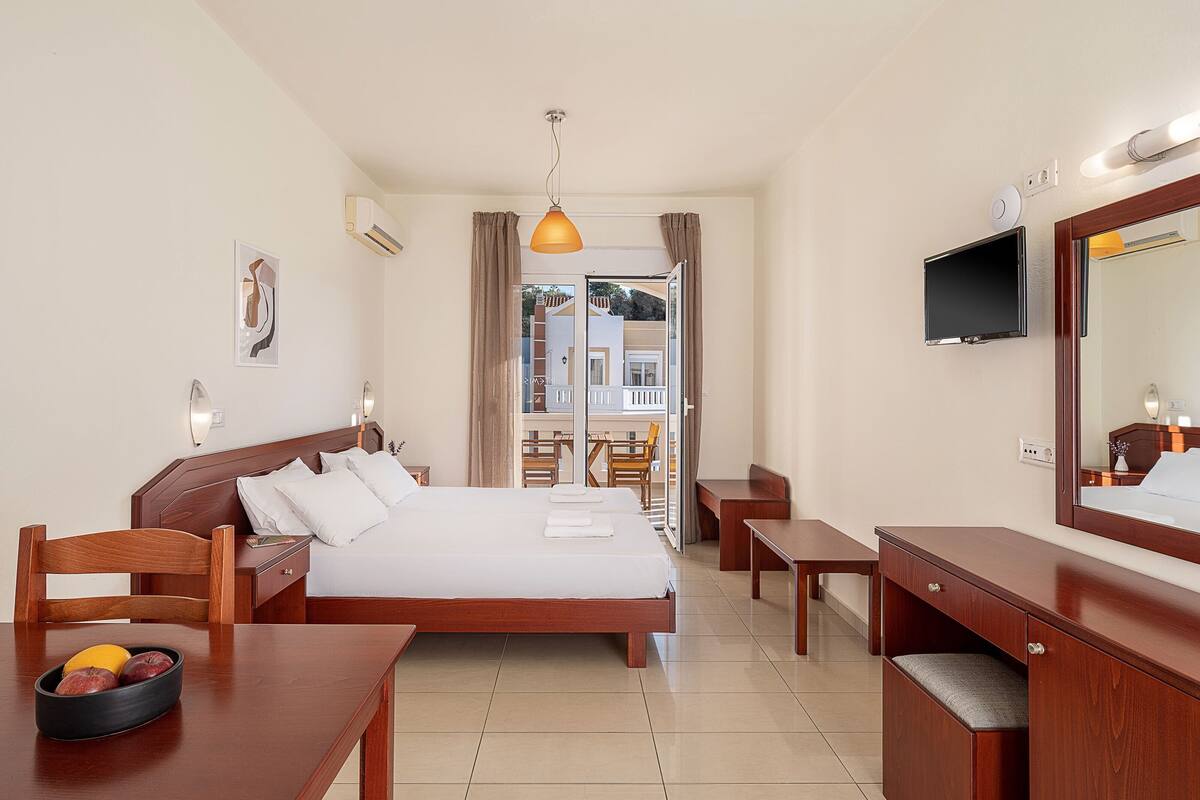 A hotel room with a bed, a desk, a chair, a TV, and a window with curtains.