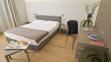 Ein Hotelzimmer mit Bett, Nachttisch mit Frühstücksangebot, Nachtschrank, einer Topfpflanze und einem Kleiderhaken.