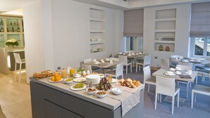 A modern dining area with multiple tables and chairs, a buffet setup with various food items, and a kitchen area with shelves and appliances. - Hotel di Varese (Varese)