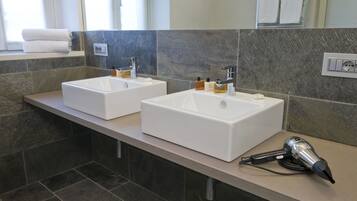 Un baño con dos lavamanos blancos, un secador de pelo en la encimera y una ventana con toallas.