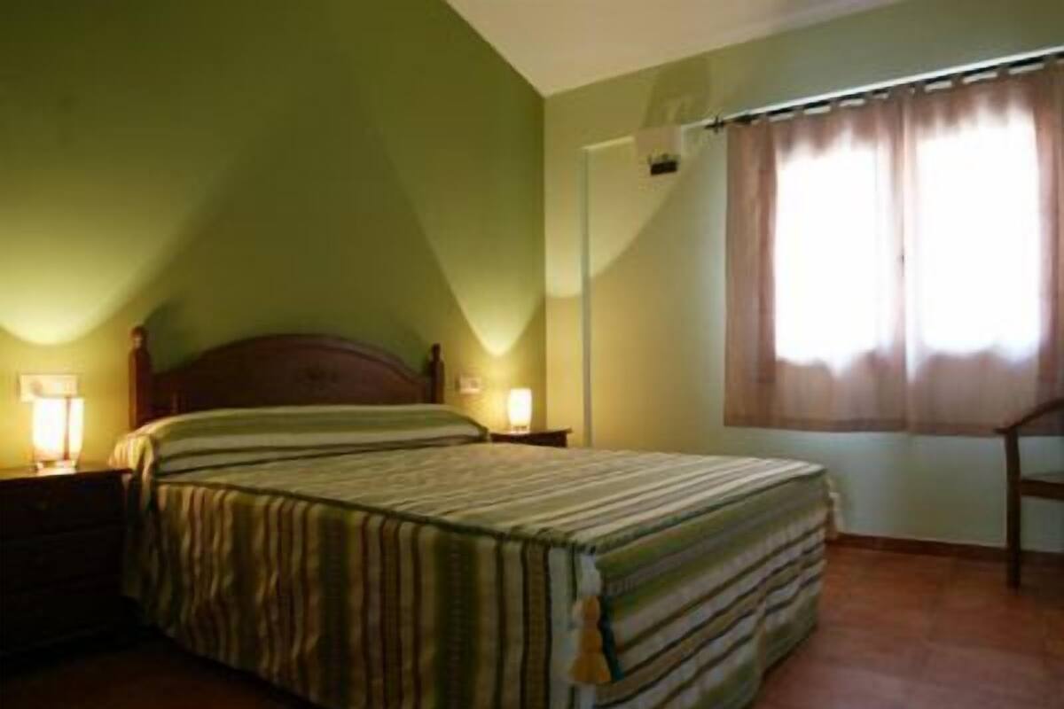 Une chambre à coucher avec un lit, des lampes de chevet, une fenêtre avec des rideaux et un plafond en pente.