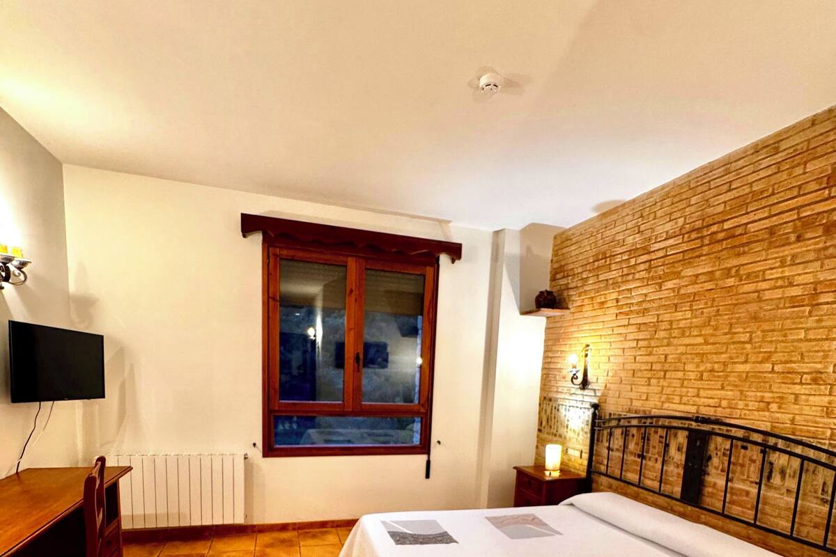 Une chambre à coucher avec un lit, un bureau, une chaise, une fenêtre et un mur en briques.
