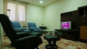 Una sala pequeña con un sofá, dos sillones, una mesa de centro, un televisor y una lámpara de pie.