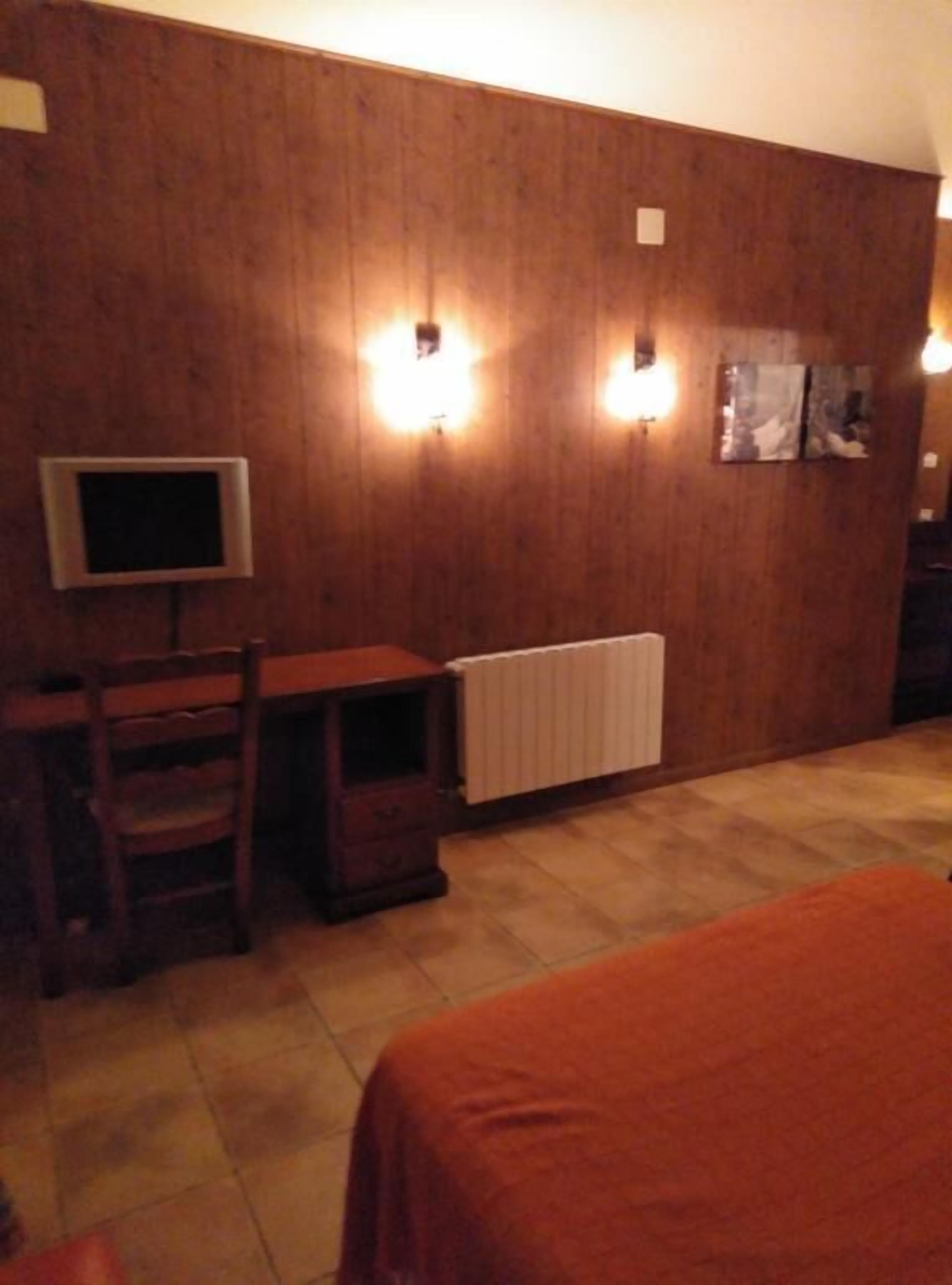 Una habitación con pared de madera, un escritorio con silla, un radiador y una cama con colcha naranja.