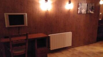 Una habitación con pared de madera, un escritorio con silla, un radiador y una cama con colcha naranja.