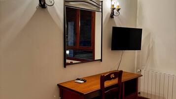 A room with a wooden desk, a chair, a television mounted on the wall, and two wall-mounted sconces.
