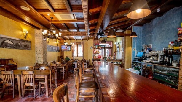 Una zona de bar con mesas y sillas de madera, una barra alargada y un puesto de barista.