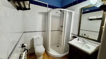 Un baño con inodoro blanco, cabina de ducha y lavamanos con espejo.