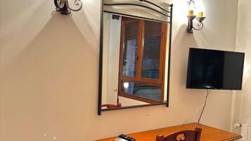 Una habitación con un escritorio de madera, una silla, un televisor de pantalla plana montado en la pared y dos apliques de pared con velas.