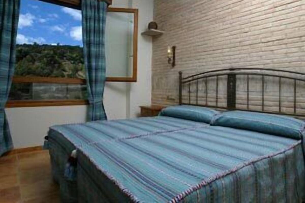 Une chambre à coucher avec un lit, une fenêtre avec des rideaux, un mur en briques et une table de chevet.