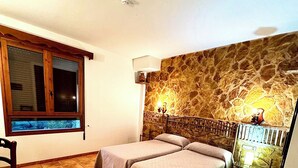 Un dormitorio con dos camas, una pared de piedra, una ventana y piso de baldosas.