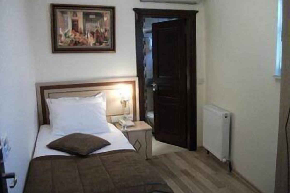 A bedroom with a bed, a nightstand, a painting on the wall, and a door.