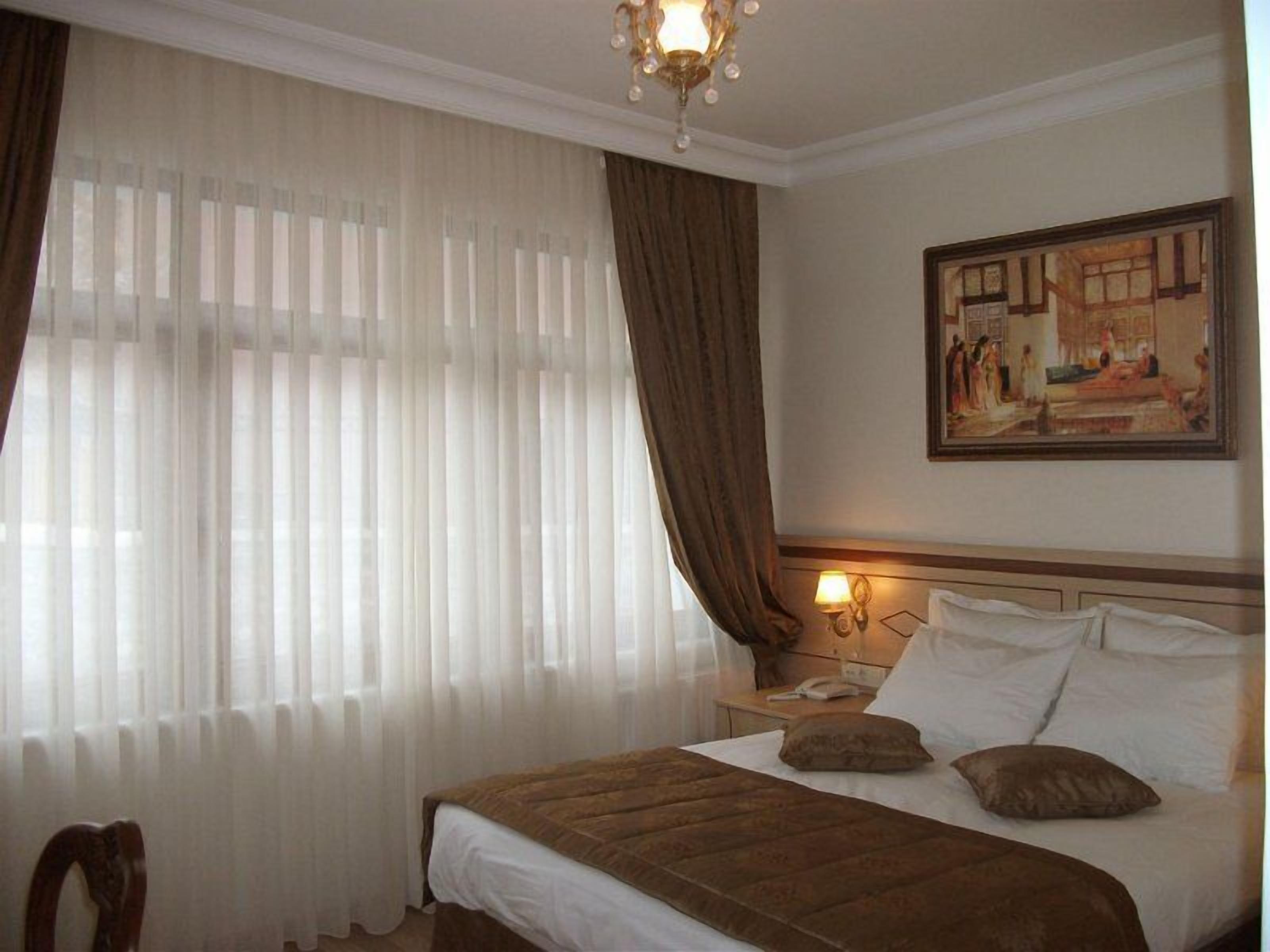 Una camera d'albergo con un letto, tende, un quadro e un comodino con una lampada.