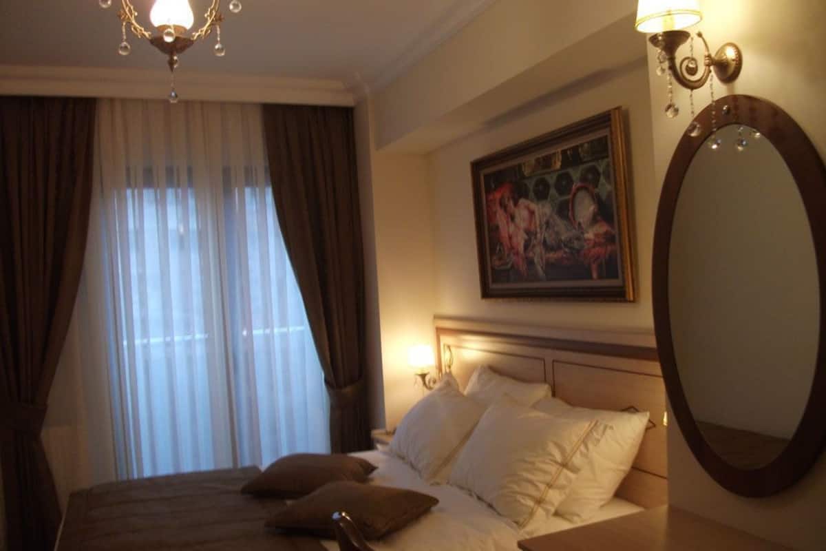 A hotel room with a bed, a nightstand, a mirror, a painting on the wall, and a chandelier.