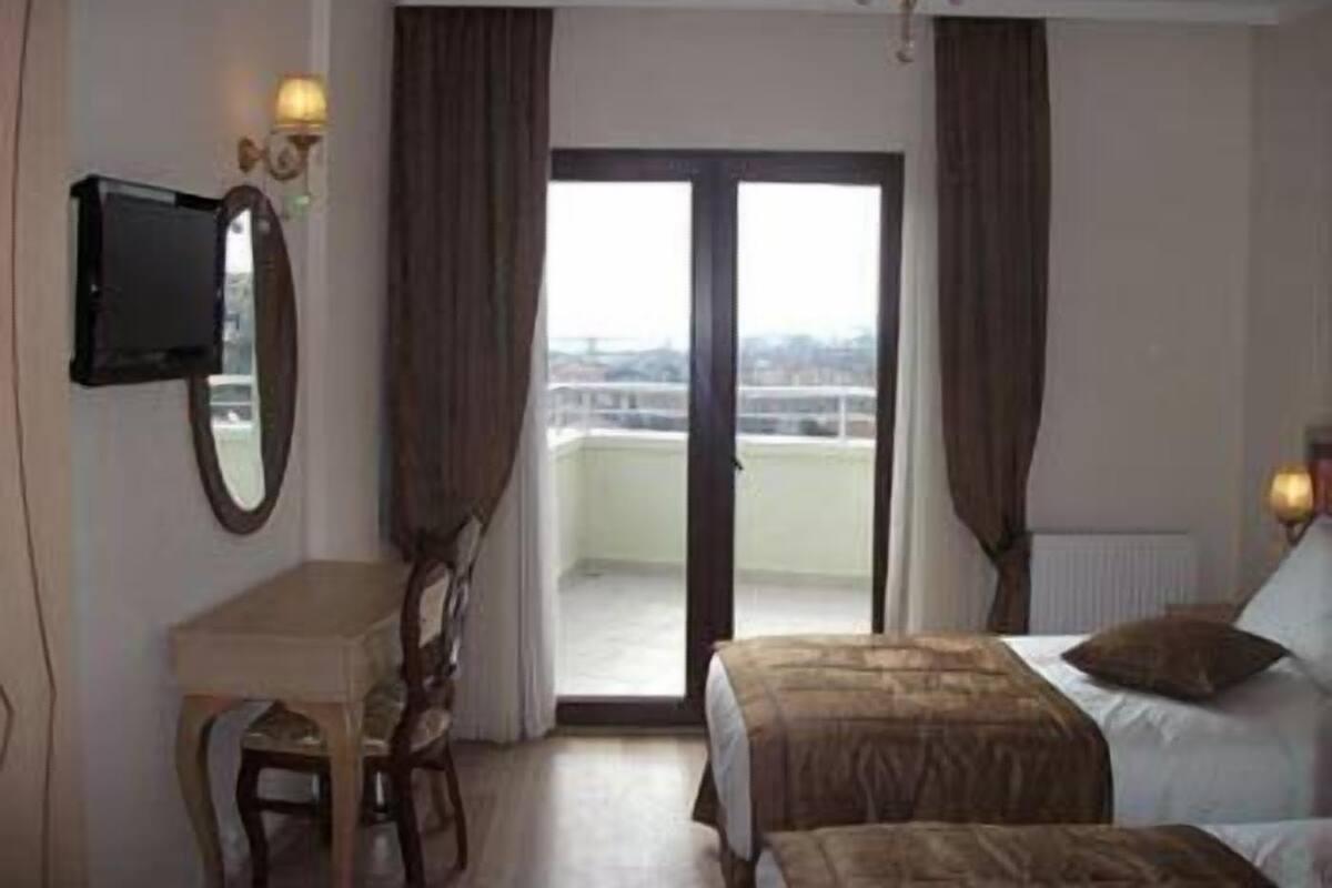 A hotel room with a bed, a desk, a chair, a television, and a balcony with curtains.