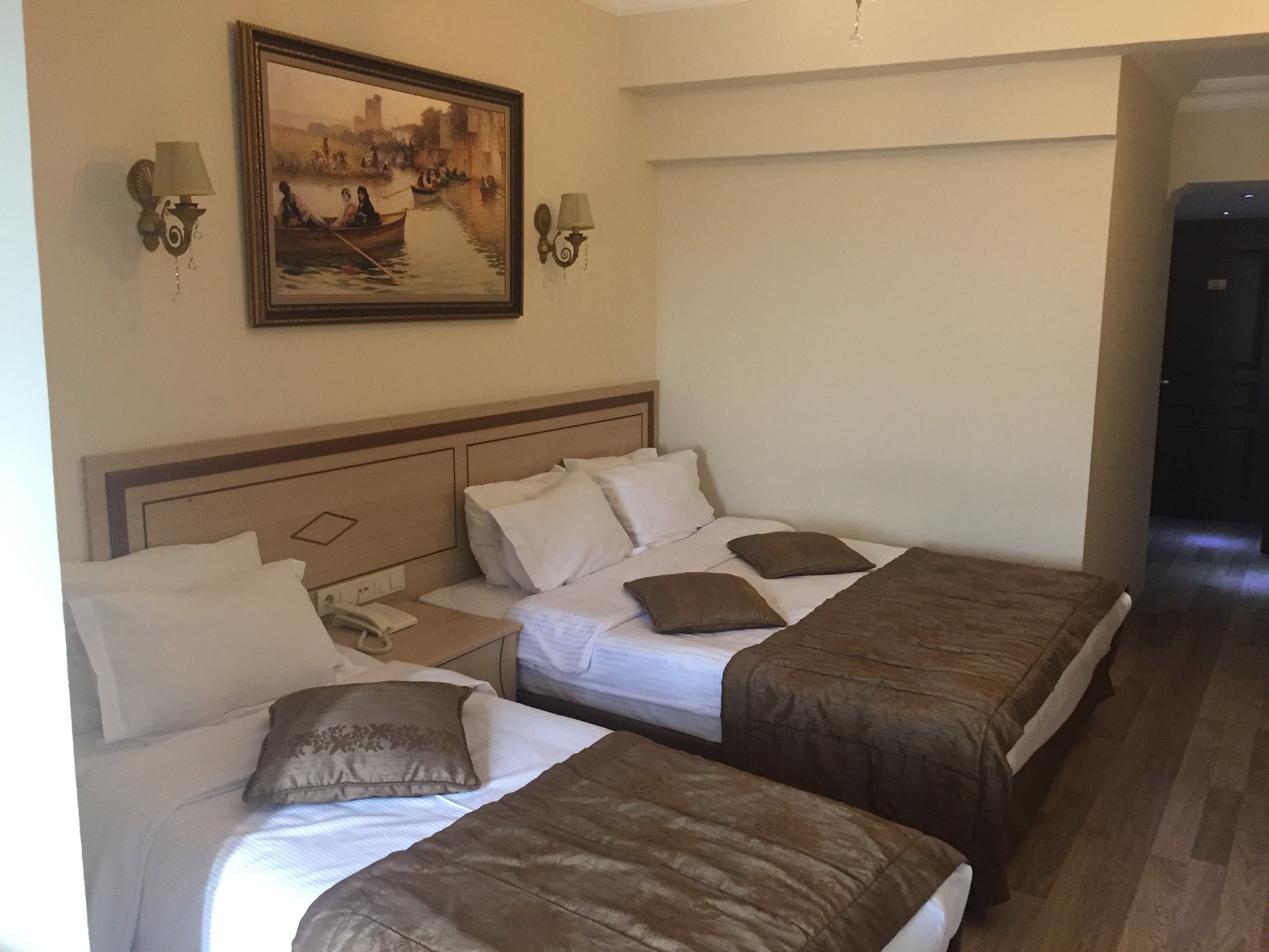 A hotel room with two beds, a painting on the wall, and a telephone on the nightstand.